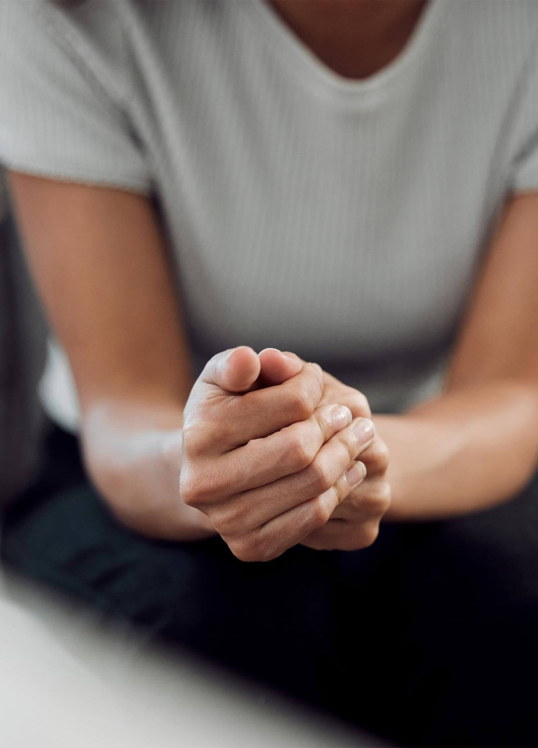 A woman holding her hands clasped together whilst sat on the sofa at a counselling session.